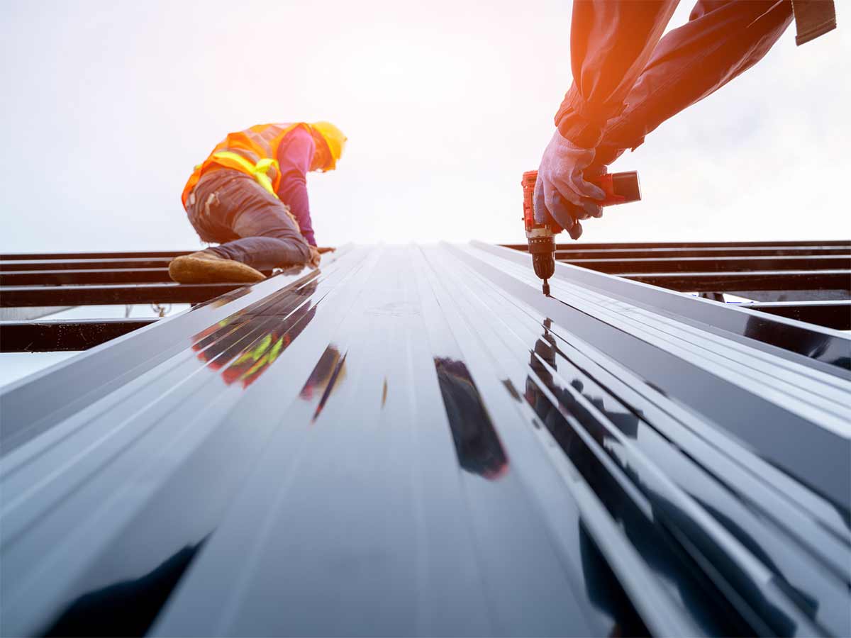 Two workers are shown installing metal onto a roof.